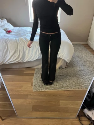 Svarta low waist bootcut jeans - Säljer ett par svarta low waist jeans med bootcut passform. Jeansen har klassisk femficksdesign och sitter tight över höfterna för att sedan bli vidare nedtill. Perfekta för en trendig och avslappnad look. Har sprätt upp sömnen längst ner men inget som syns speciellt mycket 