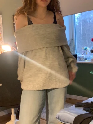 Ljusgrå off shoulder stickad tröja - Trendig ljusgrå stickad tröja med bred off shoulder-krage som ger en avslappnad och cool look. Tröjan har en oversized passform och långa ärmar. Perfekt att matcha med jeans för en casual stil.