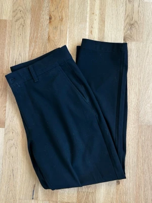 Svarta kostymbyxor från Zara med smal passform - Snygga svarta kostymbyxor med smal passform och klassiska fickor. Byxorna har hällor för bälte och stängs med knapp och dragkedja. Materialet känns mjukt och följsamt.