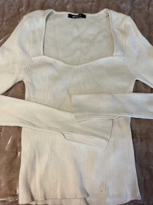 Vit ribbad topp från Gina Tricot - Trendig vit långärmad topp från Gina Tricot med ribbad struktur och markerad byst. Toppen har en fyrkantig urringning och är gjord i stretchigt, mjukt material som sitter snyggt på kroppen. Perfekt att styla med jeans eller kjol.