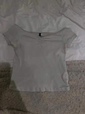 Ljusbeige ribbad topp från H&M - Snygg ljusbeige ribbad topp från H&M med korta ärmar och lätt v-ringning framtill. Toppen har en croppad passform och är tillverkad i mjuk bomullsmix. Perfekt att styla med jeans eller kjol.