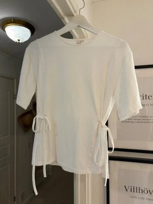 Vit t-shirt med knyt från Nelly - Snygg vit topp från Nelly med kort ärm och trendiga knytband i sidorna. Enkel och stilren design med rund halsringning, perfekt att matcha med jeans eller kjol. Mjuk och skön bomullskänsla som passar året runt. I stl xs men passar också S! Hör av dig vid funderingar💕