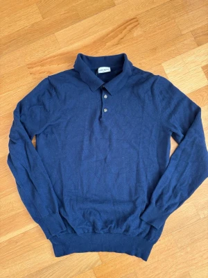 Mörkblå pikétröja från John Henric - Snygg mörkblå långärmad pikétröja från John Henric med klassisk krage och tre knappar framtill. Tillverkad i mjukt material som känns skönt mot huden. Perfekt för en stilren och avslappnad look.