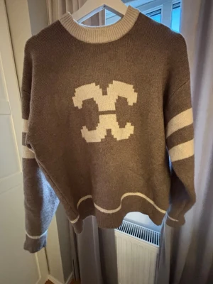 Brun stickad tröja med Off-White logga - Cool brun stickad tröja från Off-White med vit logga på bröstet och vita ränder på ärmarna. Tröjan har rund halsringning och ribbade muddar. Perfekt för dig som gillar streetwear och vill ha något unikt i garderoben. Nypris 1329!