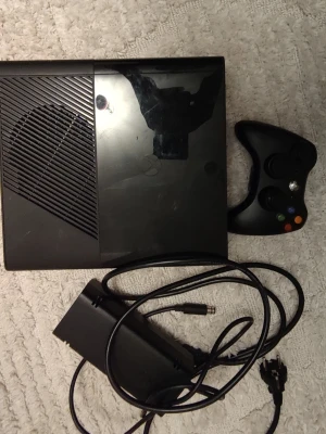 Xbox 360 Slim spelkonsol med handkontroll - Säljer en svart Xbox 360 Slim med tillhörande svart handkontroll och strömadapter. Konsolen har en stilren, blank och matt finish i plast och är perfekt för gamingkvällar med vänner. Allt du behöver för att komma igång med spelandet direkt.