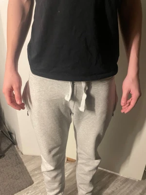 Ljusgråa mjukisbyxor - Säljer ett par ljusgråa mjukisbyxor med dragsko i midjan och smal passform. Byxorna har fickor med dragkedja på sidorna och är tillverkade i mjukt, bekvämt material. Perfekta för chill dagar eller när du vill vara extra bekväm.