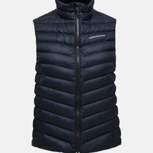 Svart dunväst från Peak Performance - Stilren svart dunväst från Peak Performance med hög krage och hel dragkedja framtill. Västen har fickor med dragkedja och på insidan. Köpt för 2100kr.