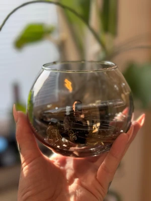 Mystery Smyckesmix i glasvas - En samling smycken i olika stilar och färger, bland annat guldfärgade kedjor, svarta detaljer och olika hängen. Allt ligger i en rund, transparent glasvas. Perfekt för dig som gillar att mixa accessoarer och vill ha en unik blandning till din smyckeskollektion.