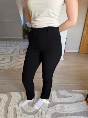 Svarta kostymbyxor med smal passform - Snygga svarta kostymbyxor med smal passform och hög midja. Byxorna har bälteshällor, diskreta sidofickor och resår baktill i midjan. Använda ett fåtal gånger. 