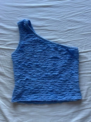 Blå oneshoulder topp  - Snygg blå topp från Things I Like Things I Love med oneshoulder-design och vågigt strukturerat tyg. 