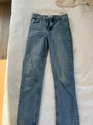 Blå raka jeans med hög midja - Snygga blå jeans med rak passform och hög midja. Klassisk femficksmodell i ett mjukt denimtyg. Perfekta till en avslappnad stil och lätta att matcha med olika toppar. Ingen synlig logga eller märke på jeansen.