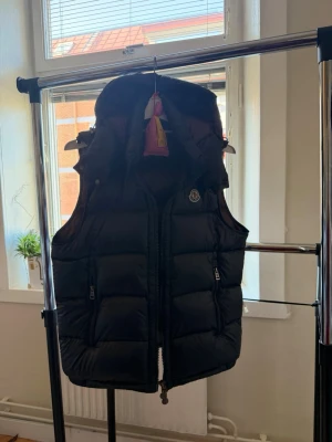 Mörkblå  Moncler väst - Snygg svart väst  från Moncler med hög krage och avtagbar huva. Västen har två dragkedjeförsedda fickor och klassisk Moncler-logga på bröstet, Västen är i riktigt bra skick.