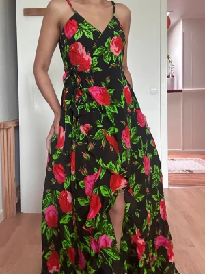 Summer floral långklänning från ASOS - Supersnygg långklänning från ASOS med svart botten och stora blommor i rött och rosa samt gröna blad. Omlottmodell med v-ringning och knyt i midjan. Perfekt för dig som vill sticka ut med färg och mönster. Luftigt material och flowig passform.