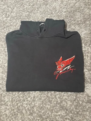 Givenchy hoodie - Svart hoodie från Givenchy i storlek L med huva och magficka. Unik broddererad logga på bröstet med texten ”Givenchy” i skrivstil. Hoodien har ribbade muddar vid ärmar och nederkant. Perfekt för dig som gillar streetwear och vill sticka ut med en unik hoodie utav kvalité. 