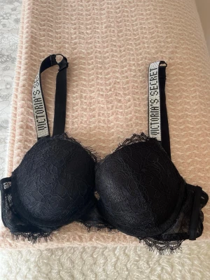 Victoria’s Secret Bh - Snygg svart bh från Victoria’s Secret med vadderade kupor och diamantdetaljer. Axelbanden är dekorerade med märkets logga i vitt och har en sportig känsla. Bh:n har en feminin design med fina spetskanter och justerbara axelband.