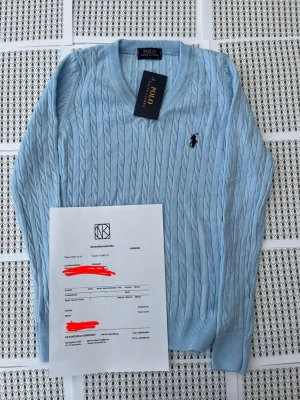Ljusblå kabelstickad tröja Polo Ralph Lauren - Snygg ljusblå kabelstickad tröja från Polo Ralph Lauren med klassisk broderad logga på bröstet. Tröjan har rund halsringning, långa ärmar och ribbade muddar vid ärmslut och nederkant. Perfekt för en stilren och avslappnad look.