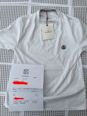 Vit Moncler t-shirt med logga - Snygg vit t-shirt från Moncler med klassisk rund hals och Monclers ikoniska logga broderad på bröstet. Tillverkad i mjuk bomull för en skön känsla och stilren look. Perfekt för dig som gillar exklusiva märken och enkel design.