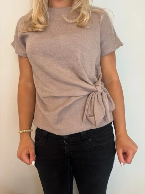 Beige topp med knyt - Trendig beige topp och korta ärmar. Snygg detalj med knyt i sidan.