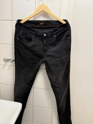 Svarta slim fit jeans från BOSS - Snygga svarta slim fit jeans från BOSS med klassisk femficksmodell och knappgylf. Jeansen har en stilren look och är tillverkade i ett mjukt bomullsmaterial med lite stretch för extra komfort. Perfekta för dig som gillar en modern och enkel stil.