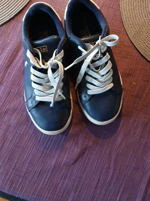 Marinblå Polo Ralph Lauren sneakers - Snygga marinblå sneakers från Polo Ralph Lauren med vita detaljer och vita snören. Klassisk låg modell med logga på sidan och vit sula. Perfekta för en clean och sportig stil. Materialet är en mix av syntet och textil.