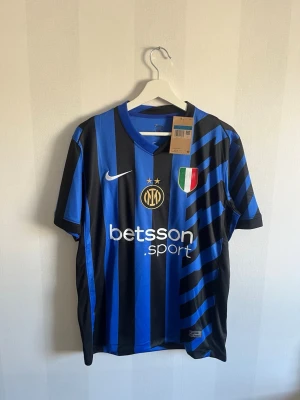 Inter Milan randig matchtröja Nike - Snygg blå och svart randig Inter Milan matchtröja från Nike med klubbmärke, sponsortryck och italienska mästarmärket på bröstet. Tillverkad i lätt polyester, perfekt för fotboll eller träning. Klassisk passform och korta ärmar.
