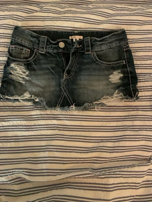 Mörkblå slitna jeanskjol med fransar - Säljer ett par mörkblå jeansshorts från Spoiled med slitna detaljer och fransig kant. Shortsen har klassiska fickor fram och bak, samt dekorativa nitar på bakfickan. Perfekta för en avslappnad och trendig look.