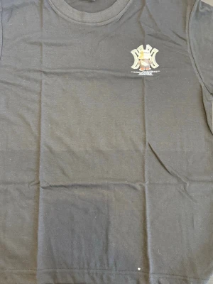 Svart t-shirt med björntryck från Niclontbear - Cool svart t-shirt från Niclontbear med ett stort tryck av en björn i hatt och sneakers på bröstet. T-shirten har rund hals och korta ärmar. Perfekt för dig som gillar streetwear och vill sticka ut med ett unikt motiv.  Storlek: Passar M–L  💬 Hör av dig vid intresse!