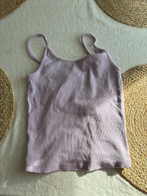 Ljuslila ribbad linnetopp - Säljer en ljuslila ribbad linnetopp med smala axelband. Toppen har en enkel och clean design som passar perfekt till sommaren. Materialet är mjukt och stretchigt för en bekväm passform. Storlek s 