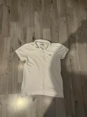 Vit pikétröja från Hampton republic  - Klassisk vit pikétröja från Hampton republic med korta ärmar och liten logga på bröstet. Tröjan har krage och knappar framtill, perfekt för en clean och stilren look. Tillverkad i mjuk bomull som känns skön mot huden.