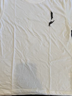 Vit t-shirt med svart konsttryck - Vit t-shirt med ett unikt svart konsttryck på framsidan som föreställer en hand och ett ansikte. T-shirten har klassisk passform och rund hals. Perfekt för dig som gillar minimalistisk och stilren design.