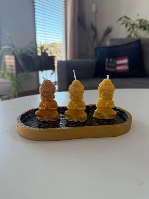 Buddha ljus i set med bricka - Finns i andra färger - Tre små ljus i form av sittande Buddhafigurer som dekoration till hemmet eller för meditation. Ljusen har tydliga vekar och brickan har en strukturerad yta.Går att få inslaget i present om det önskas 