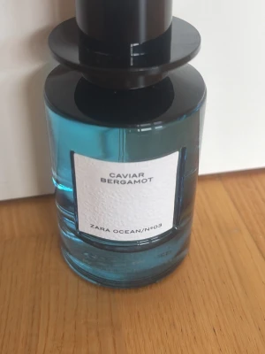 Zara Caviar Bergamot parfym - Fräsch parfym från Zara i serien Ocean N°03 med doft av caviar och bergamott. Flaskan är cylindrisk i blått glas med svart lock och vit etikett framtill. Perfekt för dig som gillar marina och citrusaktiga dofter.