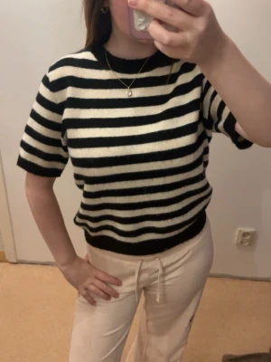 Randig stickad topp - Stickad tröja med breda svarta och vita horisontella ränder. Modellen har korta ärmar, rund hals och ribbade muddar vid ärmslut och nederkant. Materialet är mjukt och fluffigt, vilket ger en avslappnad och trendig vibe.