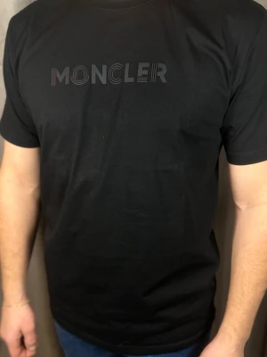 Svart  t-shirt med logga - . Klassisk passform och rund halsringning. Perfekt till jeans eller shorts för en clean och stilren look.