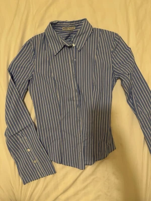 Blåvit randig skjorta från Bershka  - Snygg blå skjorta med vita vertikala ränder från Bershka. Tillverkad i bomull för en bekväm känsla och stilren look. Har använt bara en gång och det finns kvittot