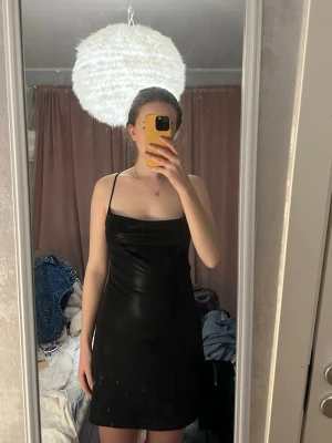 Svart kort klänning med öppen rygg - Säljer en svart kort klänning med tunna axelband och snygg öppen rygg med korsade band. Klänningen har en enkel, stilren design och sitter figurnära. Perfekt för dig som gillar minimalistisk stil.