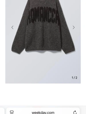 Mörkgrå stickad tröja Weekday - Mörkgrå stickad tröja från Weekday med oversized passform och svart texten 'ROMANCER' över bröstet. Tröjan har långa ärmar och är gjord i ett mjukt, luddigt material som ger en mysig känsla. Perfekt för dig som gillar statement-plagg.