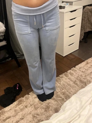 Ljusblå mjukisbyxor Juicy Couture - Säljer ett par ljusblå mjukisbyxor från Juicy Couture i supermjuk velour. Byxorna har utsvängda ben, bred linning med dragsko och stora fickor framtill. Perfekta för en chill och trendig look.