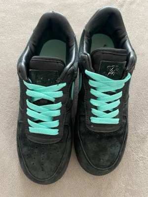 Nike Air Force 1s - Säljer ett par Nike Air Force 1 sneakers i svart mocka med turkosa skosnören och turkos Swoosh i läder.Ser utnötta ut på små ställen märks inte.
