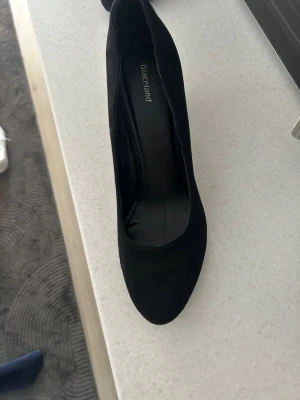 Svarta pumps från Graceland - Stilrena svarta pumps från Graceland med rundad tå och bred klack. Skorna är tillverkade i ett mockaliknande material som ger en mjuk känsla. Perfekta för dig som vill ha en klassisk och enkel look.