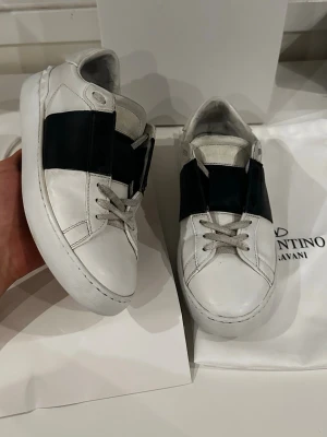 Valentino opens - Vita sneakers med svart detalj från Valentino Garavani i kalvskinn, storlek EU 41. Skorna är i mycket bra skick utan några defekter. Nypris ligger på 7280 kr, men säljs nu för 1199 kr. Tillbehör som medföljer är originalpåse, dustbag och originallåda.  Kolla gärna in profilen också, där finns flera märkeskläder och skor – du hittar säkert något mer som passar 😉💯 Hör av dig om du undrar något!