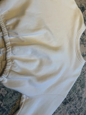 Vit sweatshirt med resår - En vit croppad sweatshirt med rund hals och resår i midjan samt vid ärmsluten. Tröjan har en avslappnad passform och är tillverkad i mjukt material, perfekt för en chill och stilren look. Använd fåtal gånger