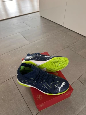 Puma blå/gröna fotbollsskor strl 40.5 - Säljer ett par snygga Puma fotbollsskor i marinblått med limegröna detaljer och vit logga. Helt nya! Använd 1-2 gånger.