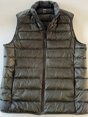 Grön dunväst från Uniqlo Ultra Light - Snygg grön dunväst från Uniqlo Ultra Light Down-serien. Västen har en hög krage, dragkedja framtill och quiltad design. Tillverkad i lätt och smidigt material som håller värmen utan att kännas tung. Perfekt för lager-på-lager och enkel att packa ner.