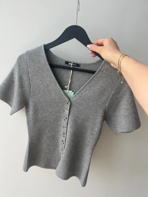 Grå v-ringad topp från Gina Tricot - Stilren grå topp från Gina Tricot med v-ringning och korta ärmar. Aldrig använd, köpt för 399kr. Säljer för 250 kr.