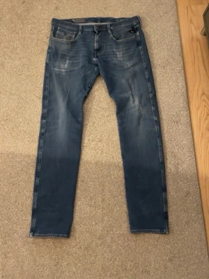 Blå slim fit jeans med slitningar - Snygga blå slim fit jeans med lätt slitna detaljer framtill och klassiska fem fickor. Jeansen har normal midja och raka ben. Perfekta för en avslappnad och trendig look.