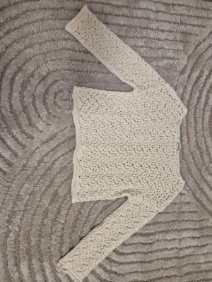 Vit stickad spetsmönstrad tröja i storlek S - Snygg krämvit stickad tröja med spetsmönster och långa ärmar. Tröjan har en rak passform och är perfekt med och utan linne under. Mjukt material och diskret vågig kant nedtill ger en extra touch. Storlek S