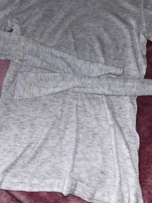 Ljusgrå ribbad tröja H&M  - Ljusgrå långärmad tröja från H&M med ribbad struktur. Tröjan har en rund halsringning och är tillverkad i ett mjukt, stretchigt material som sitter skönt på kroppen. Perfekt att matcha med jeans eller kjol. Aldrig använd 