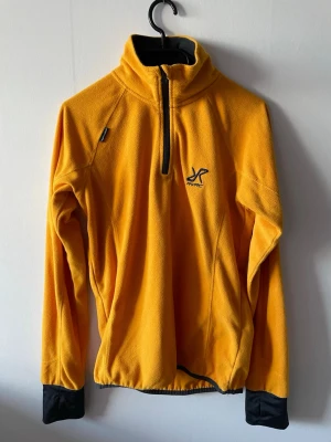 Gul fleecejacka från RVRC med halv dragkedja - Snygg gul fleecejacka från RVRC med halv dragkedja framtill och hög krage. Tröjan har svarta muddar vid ärmsluten och broderad logga på bröstet. Perfekt för lager-på-lager och outdoor. Tillverkad i mjukt fleecematerial som håller dig varm.