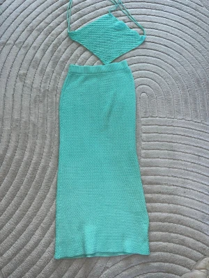Turkos stickad kjolset - Säljer ett turkost stickat set med en lång kjol och matchande trekantsformad topp med tunna band. Setet har en trendig virkad look och är perfekt för dig som gillar färg och unika plagg. Materialet känns mjukt och luftigt, perfekt för sommaren. Kjolen har några trådar 
